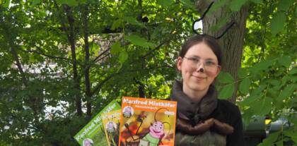Person mit Insektenkostüm hält Kinderzeitschriften im Wald.