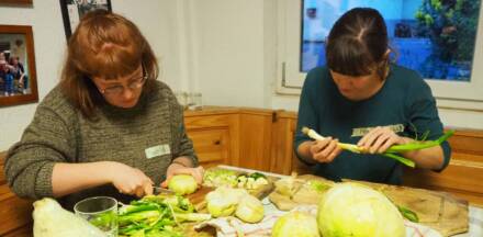 Personen schneiden Gemüse am Tisch.