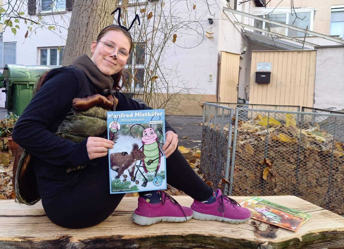 Manfred Mistkäfer hält Manfred Mistkäfer-Magazin vor Herbstkulisse.
