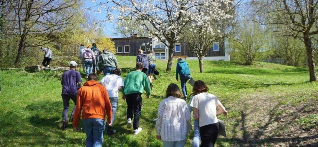 Gruppe geht durch Frühlingslandschaft Richtung Gebäude.