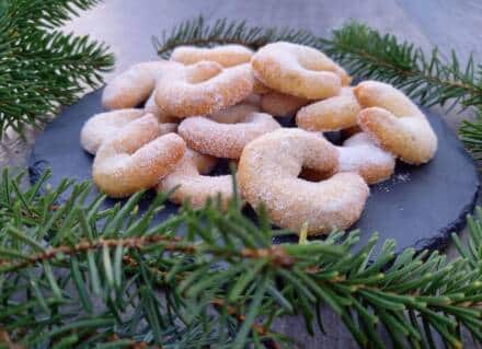 Zuckerbestäubte Kekse auf Schieferplatte mit Tannenzweigen.
