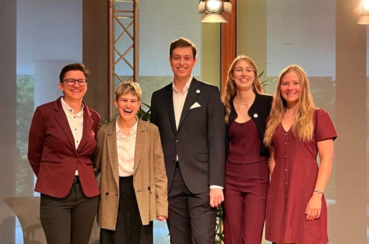 Fünf Personen in Businesskleidung stehen zusammen auf der Bühne.