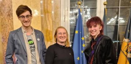 Drei lachende Personen vor EU-Flagge.