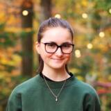 Lächelnde Person im Grünen vor Herbsthintergrund.